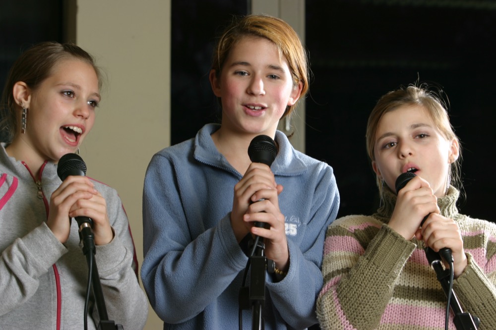 Drei Schülerinnen singen in Mikrofone