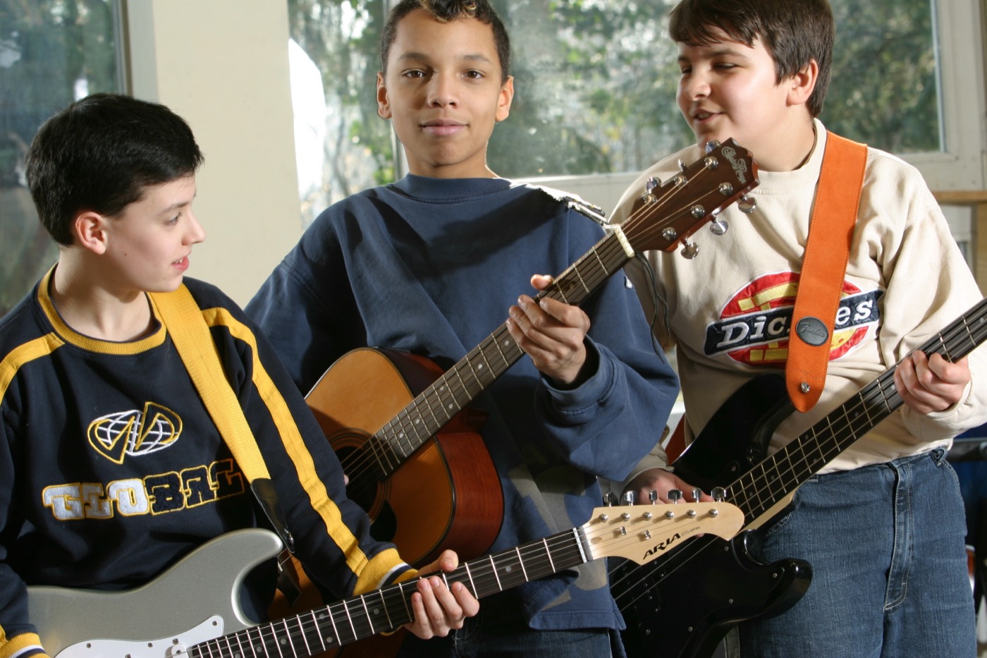 Drei Schüler mit Akustikgitarre, E-Gitarre und Bass